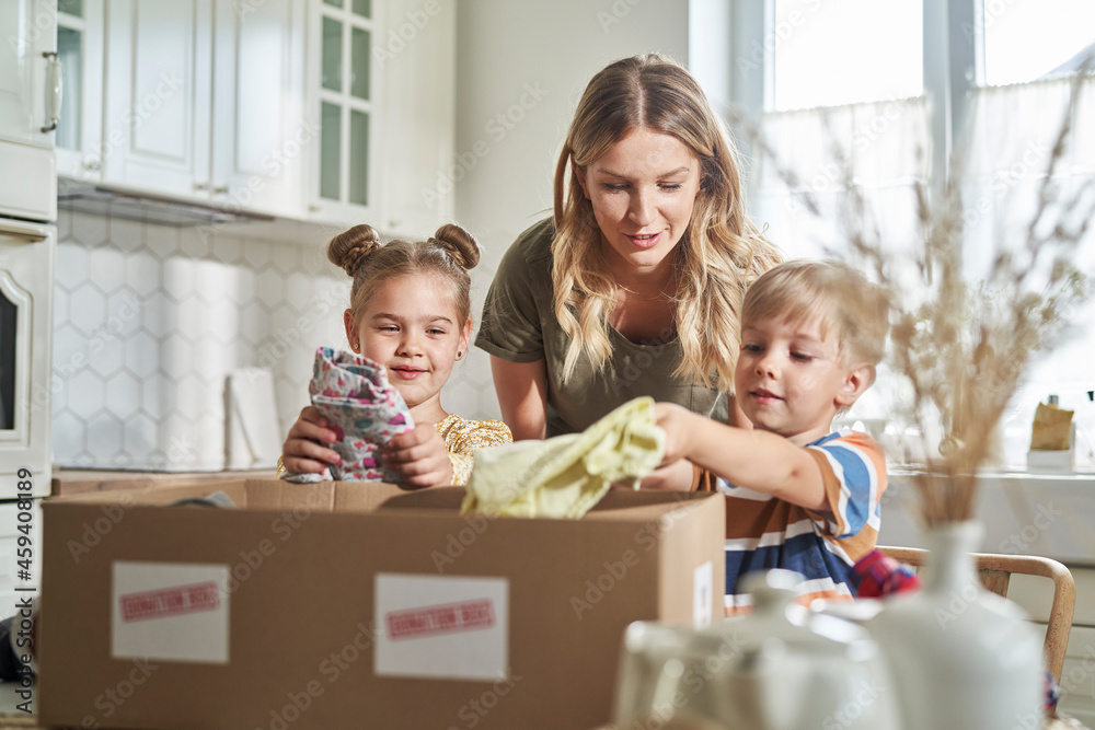 Woman talking with children packing clothes in donation box at home Woman talking with children packing clothes in donation box at home