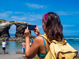 Una chica joven tomando una foto con su telefono movil en la playa de Las Catedrales de Galicia