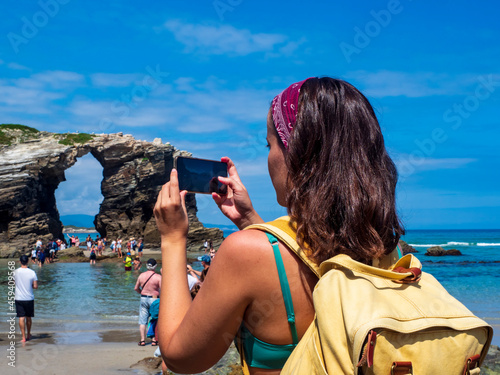 Una chica joven tomando una foto con su telefono movil en la playa de Las Catedrales de Galicia photo