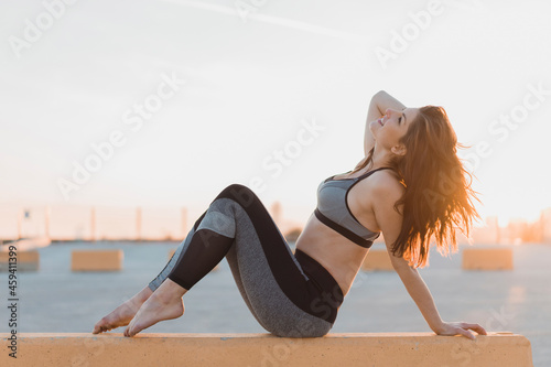 Woman in sports clothing sitting on retaining wall during sunset