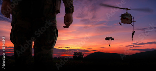 Silhouette back side view soldier paarachute and helicopter soldier under army training and big tree at sunset mountain twilight sky background.