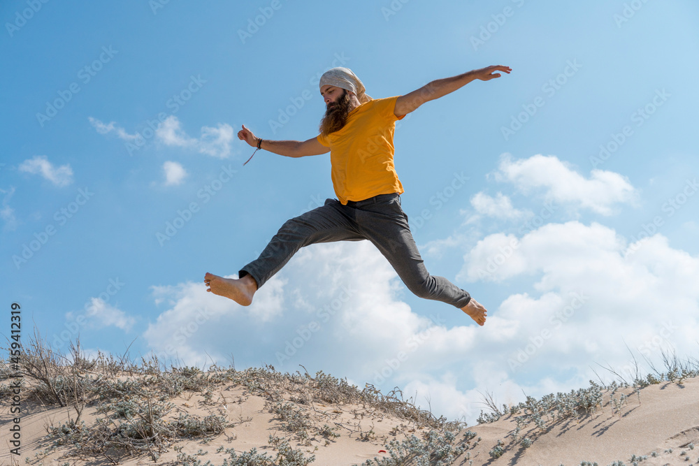 Carefree man with arms outstretched jumping on sand at beach Carefree man with arms outstretched jumping on sand at beach