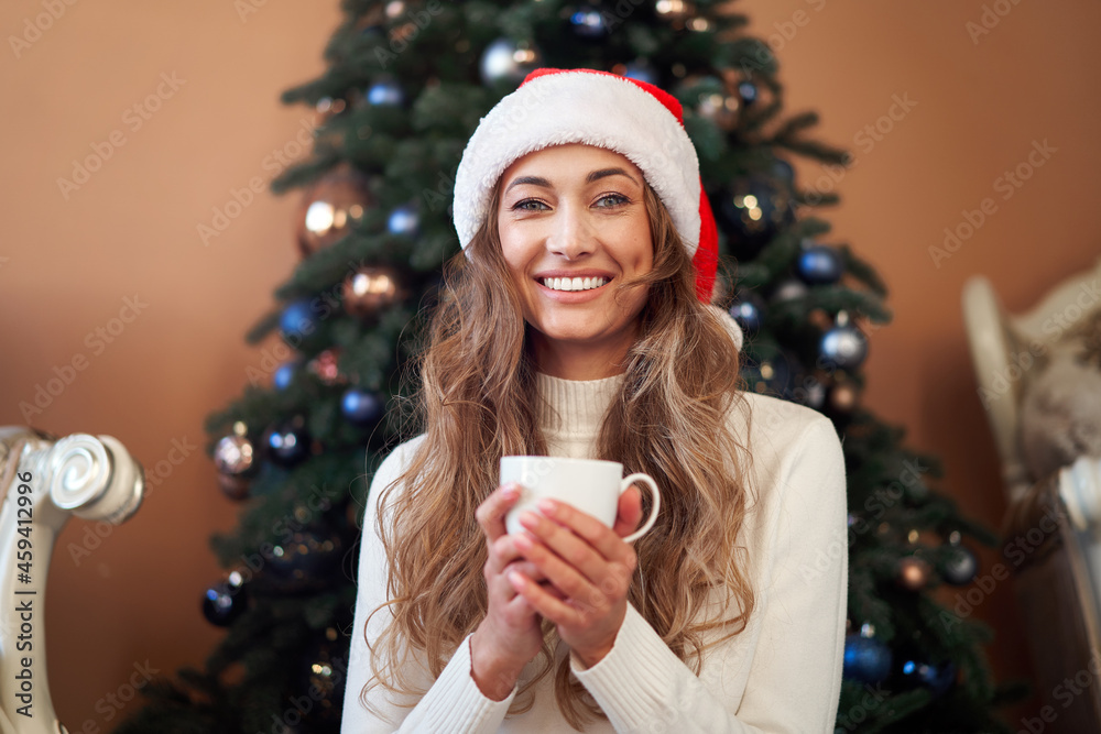 Christmas. Woman dressed white sweater Santa hat and jeans sitting on the floor near christmas tree with present box Christmas. Woman dressed white sweater Santa hat and jeans sitting on the floor near christmas tree with present box