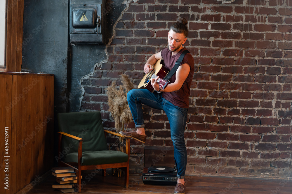 Fototapeta premium Man with acoustic guitar against brick wall playing music singing songs enjoy life Medium shoot