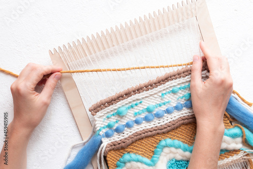 Female hands weave beautiful handmade wall hanging on white background.