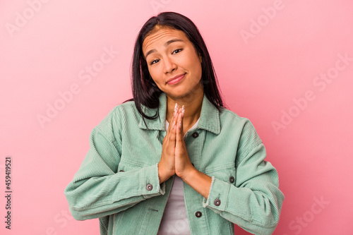 Young latin woman isolated on pink background holding hands in pray near mouth, feels confident.