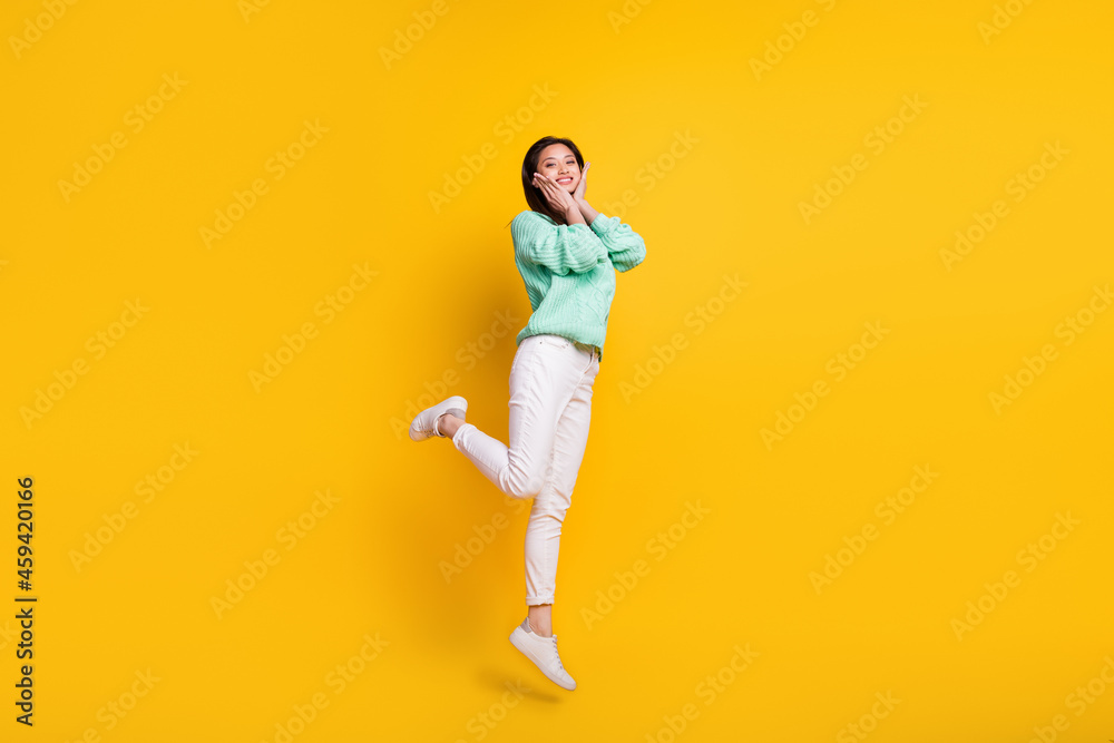 Full size photo of pretty nice cute woman jump up air smile hold hands face cheeks isolated on yellow color background