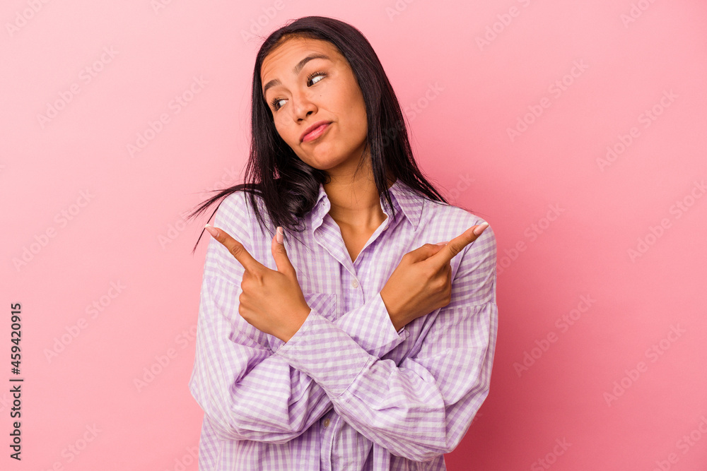 Young latin woman isolated on pink background points sideways, is trying to choose between two options. Young latin woman isolated on pink background points sideways, is trying to choose between two options.