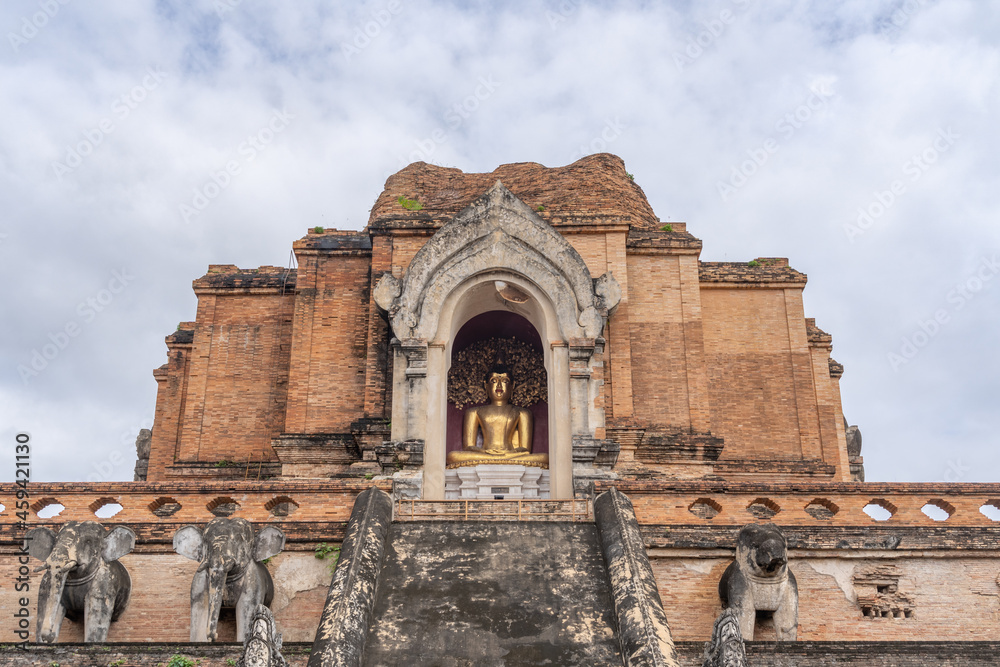 Landscape view of famous historical Lanna stupa with golden buddha statue in niche, Wat Chedi Luang buddhist temple, Chiang Mai, Thailand