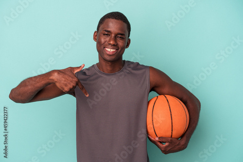 Young African American man playing basketball isolated on blue background person pointing by hand to a shirt copy space, proud and confident © Asier