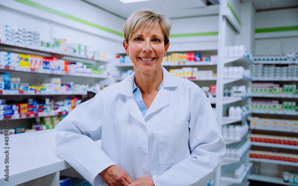 Smiling caucasian senior pharmacist leaning against counter in drugstore pharmacy 