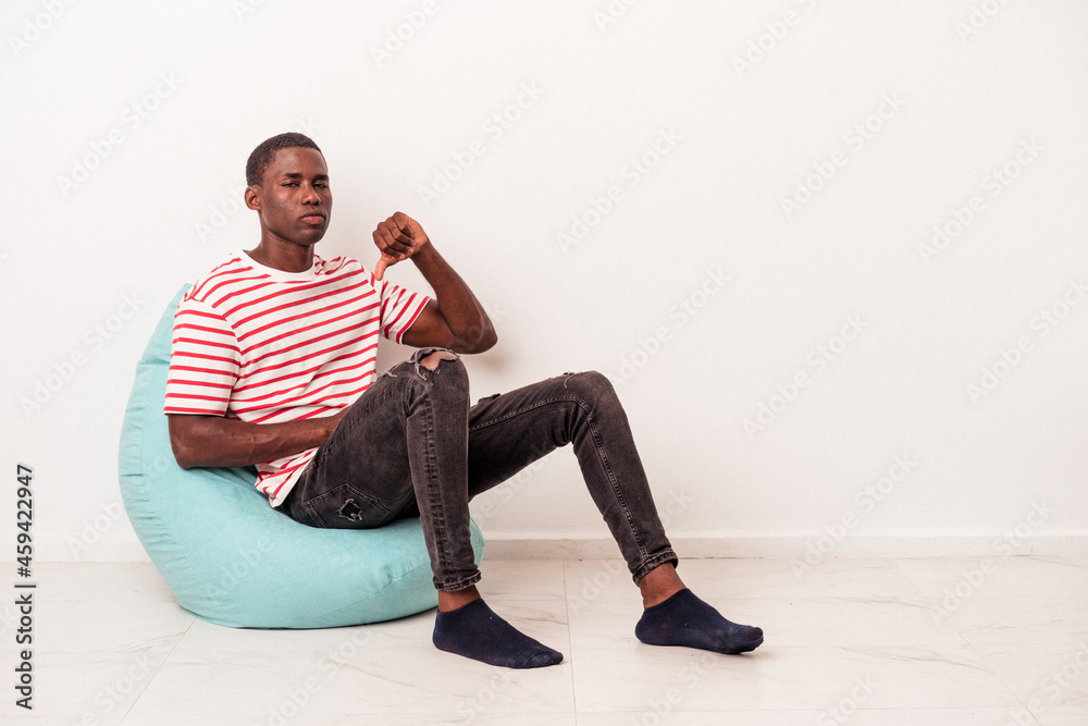 Young African American man sitting on a puff isolated on white background showing a dislike gesture, thumbs down. Disagreement concept.