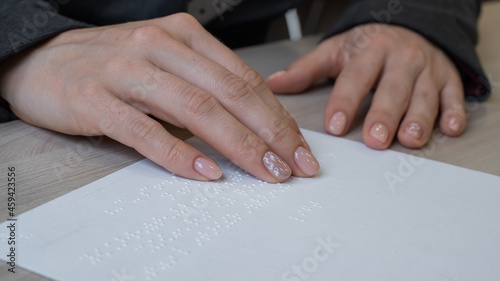Close-up woman reads the text to the blind. Woman's hands on paper with braille code.