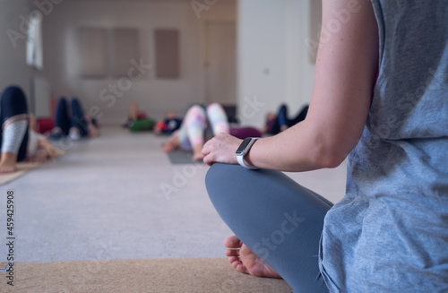 Back shot of an unrecognizable yoga teacher, seated, looking at her students lying on the floor.