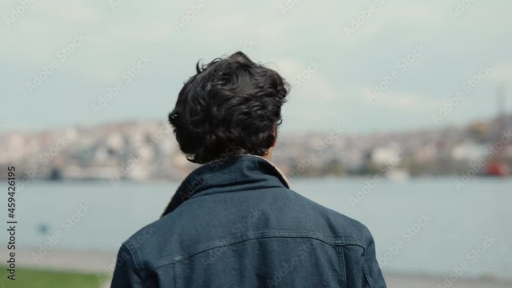 Back view of arabian man walking outdoors near city river Back view of arabian man walking outdoors near city river