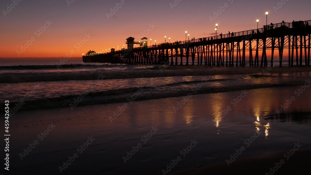 Pier silhouette Oceanside California USA. Pacific ocean tide tropical beach. Summertime gloaming atmosphere. Purple aesthetic gradient, calm twilight sky, pink violet dusk. Lights reflection in water.