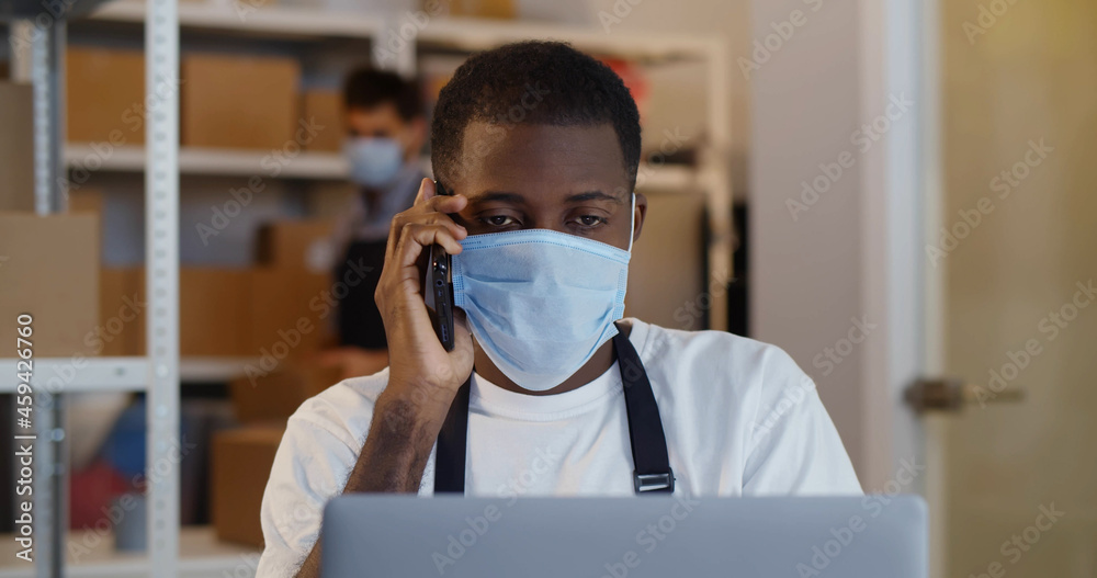 African man online seller in safety mask confirming orders from customer on phone African man online seller in safety mask confirming orders from customer on phone