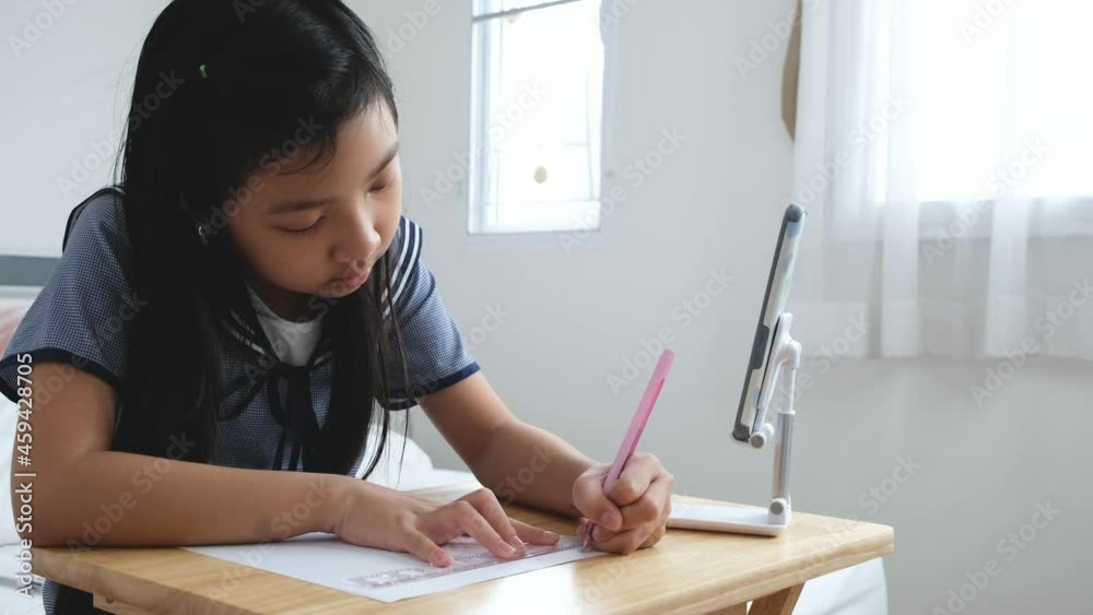 Asian child girl studying at home online on her smartphone during the new normal of the COVID-19 pandemic Asian child girl studying at home online on her smartphone during the new normal of the COVID-19 pandemic