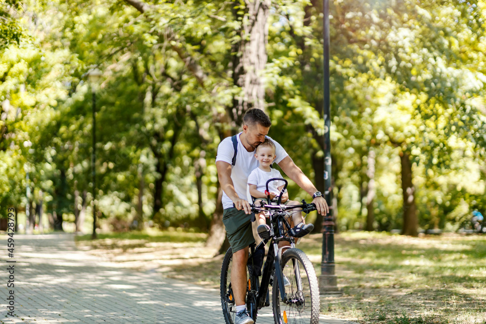 An active family day in nature. A father and son ride a bike through the woods on a sunny summer day. A cute boy is sitting in a bicycle basket while he rides a bicycle. They enjoy the ride An active family day in nature. A father and son ride a bike through the woods on a sunny summer day. A cute boy is sitting in a bicycle basket while he rides a bicycle. They enjoy the ride