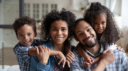 Bild auf Leinwand Head shot portrait of African American parents piggy backing kids, smiling young