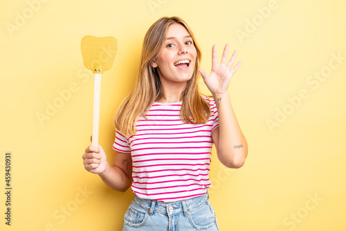 pretty blonde girl smiling happily, waving hand, welcoming and greeting you. kill flies concept photo