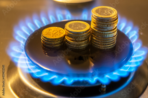 Gas stove lit, with stacks of coins above it. Increase in gas costs and tariffs. 