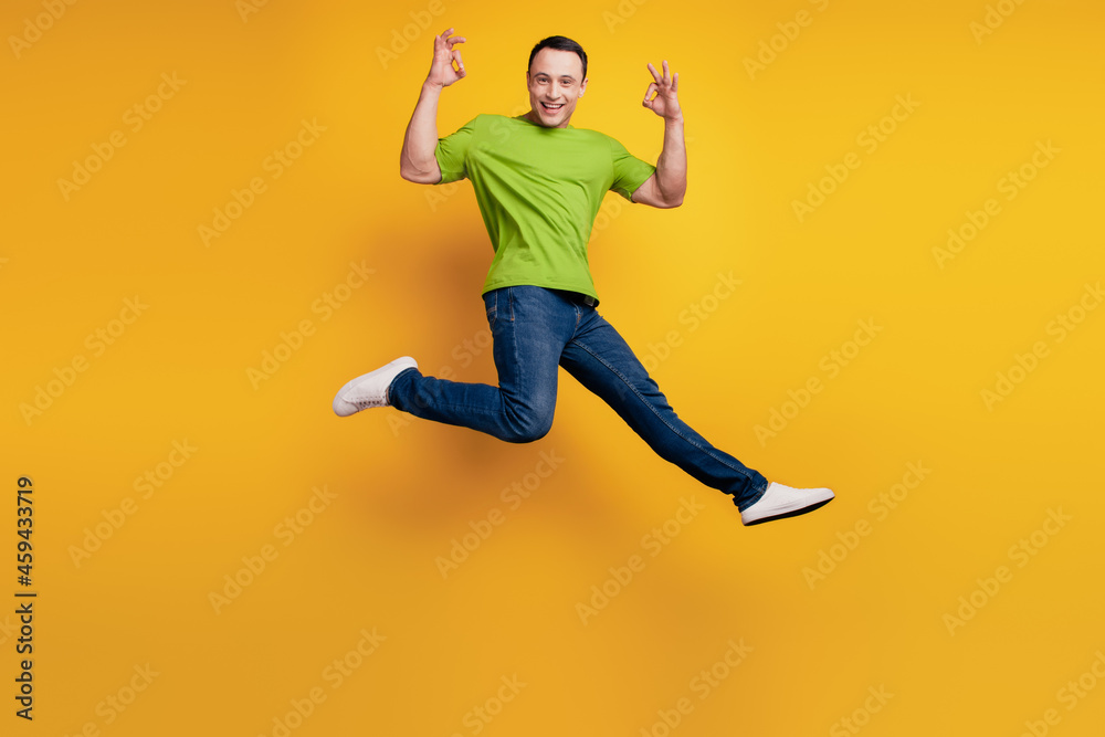 Portrait of sportive excited guy jump raise hand show okey on yellow wall