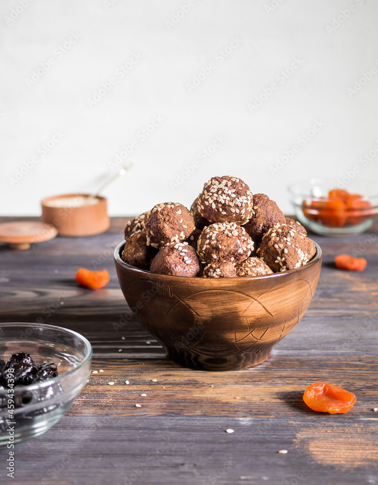 Brown.vegetarian sweets decorated with sesame seeds and carob powder in a ceramic bowl on the table along with the ingredients. Energy balls. Raw food sweets. Proper nutrition. Brown.vegetarian sweets decorated with sesame seeds and carob powder in a ceramic bowl on the table along with the ingredients. Energy balls. Raw food sweets. Proper nutrition.