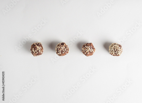 Brown vegetarian candies (energy balls) decorated with cocoa and sesame seeds lie in a row one after another. Raw food sweets. Gray background. Proper nutrition. View from above. Flat lay.