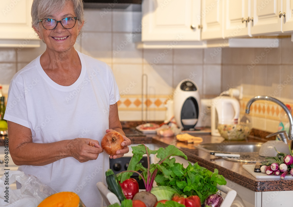 Beautiful senior woman in the home kitchen preparing vegetables. Fresh raw harvested on the table Beautiful senior woman in the home kitchen preparing vegetables. Fresh raw harvested on the table