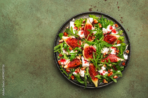 Fig salad with white cheese, walnuts, arugula and jam dressing on rust green background, top view, copy space