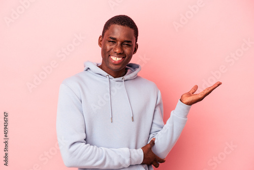 Young African American man isolated on pink background showing a copy space on a palm and holding another hand on waist.