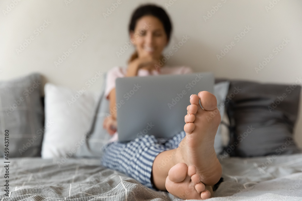 Crop close up of young woman sit relax at home on bed use laptop gadget. Closeup of female legs feet. Housewife rest on couch browse internet on computer device. Relaxation, technology concept. Crop close up of young woman sit relax at home on bed use laptop gadget. Closeup of female legs feet. Housewife rest on couch browse internet on computer device. Relaxation, technology concept.
