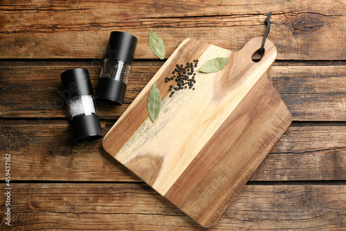 Cutting board and condiments on wooden table, flat lay. Cooking utensil
