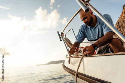 Young african american sailor tying ropes on sailboat in the sea on sunset photo