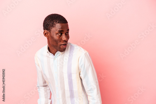 Young African American man isolated on pink background looks aside smiling, cheerful and pleasant.