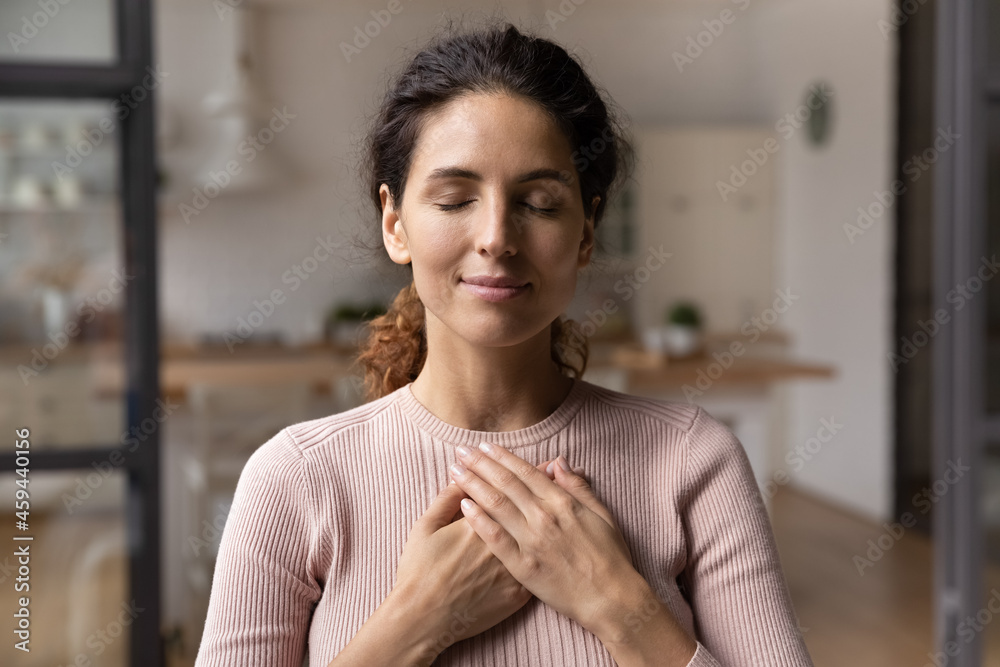 Close up of calm young Caucasian woman hold hands on heart chest feel grateful and thankful. Happy millennial female show gratitude, love and care, pray or visualize. Religion, faith concept. - obrazy, fototapety, plakaty 
