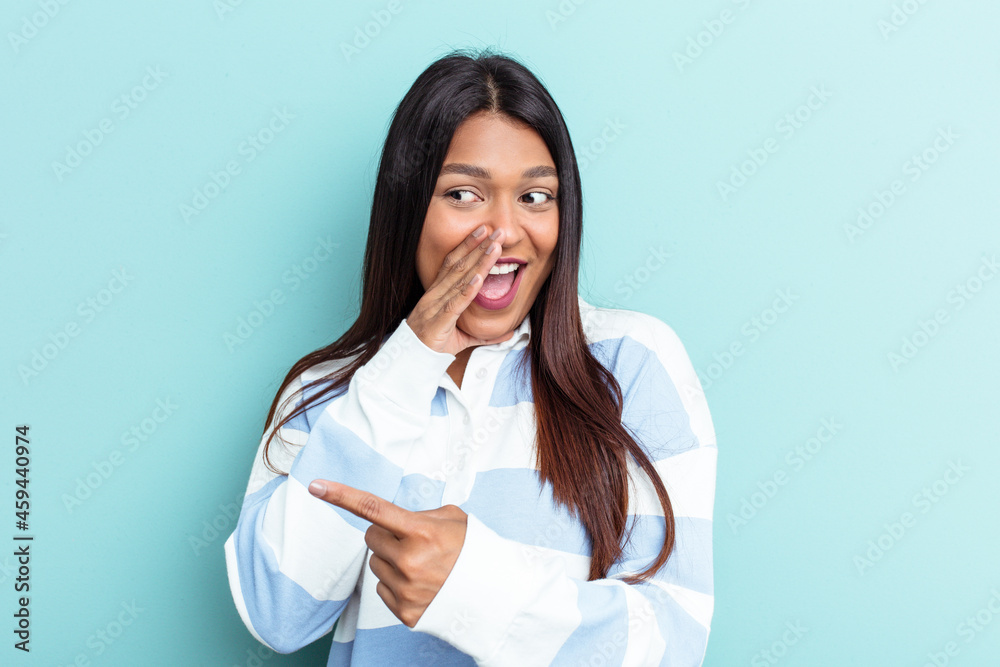 Young Venezuelan woman isolated on blue background saying a gossip, pointing to side reporting something. Young Venezuelan woman isolated on blue background saying a gossip, pointing to side reporting something.