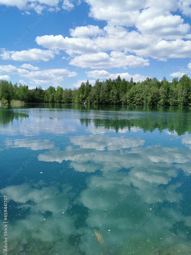 Fototapeta premium The shore of the lake is bright with clear water, in which you can see the marble on the bottom and reflect the sky with clouds, in the mountain park Ruskeala.