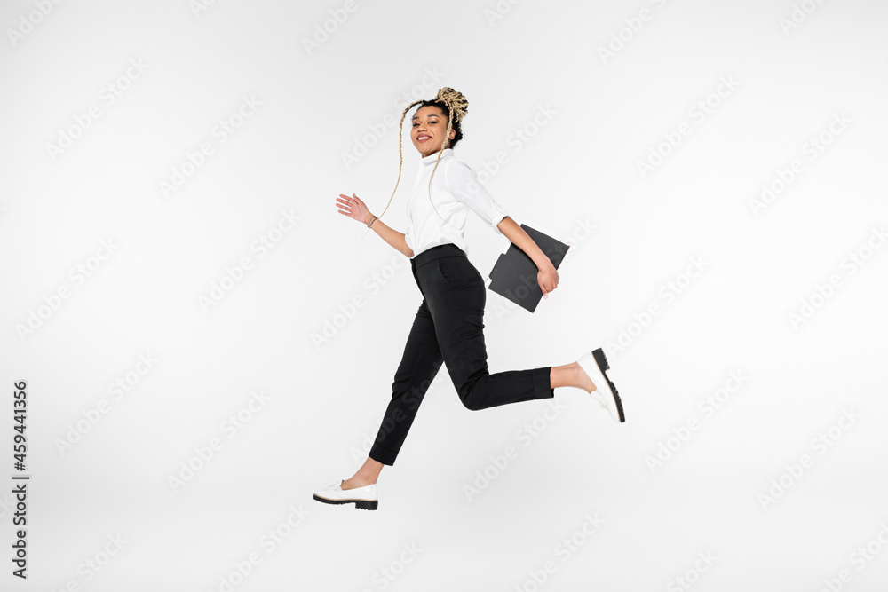 joyful african american businesswoman smiling at camera while running in levitation isolated on white