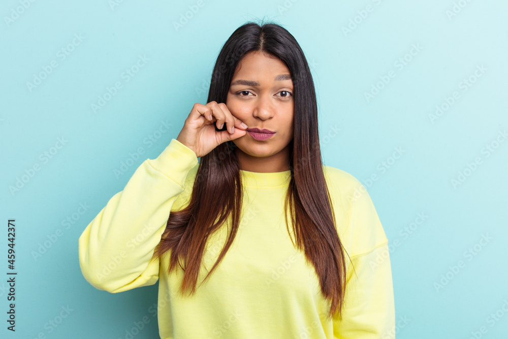 Young Venezuelan woman isolated on blue background with fingers on lips keeping a secret. Young Venezuelan woman isolated on blue background with fingers on lips keeping a secret.