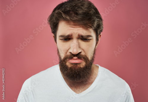 bearded man in a white t-shirt hand gestures anger pink background