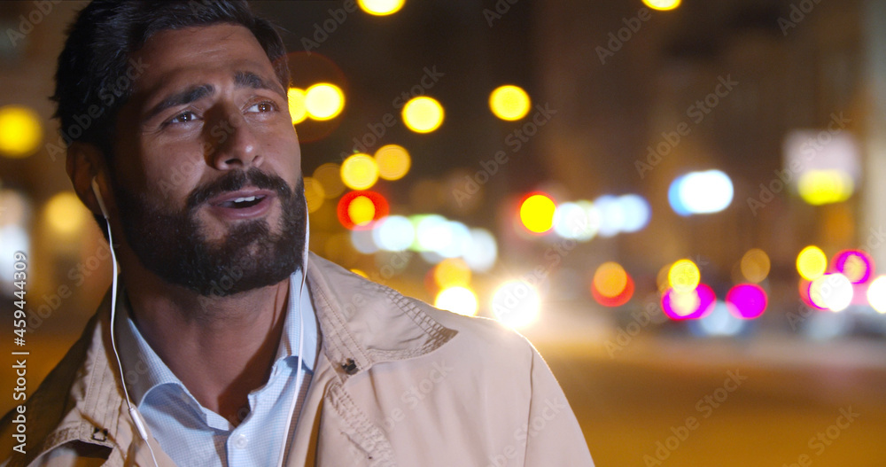 Obraz premium Bokeh shot of handsome man listening to music in earphones and singing outdoors