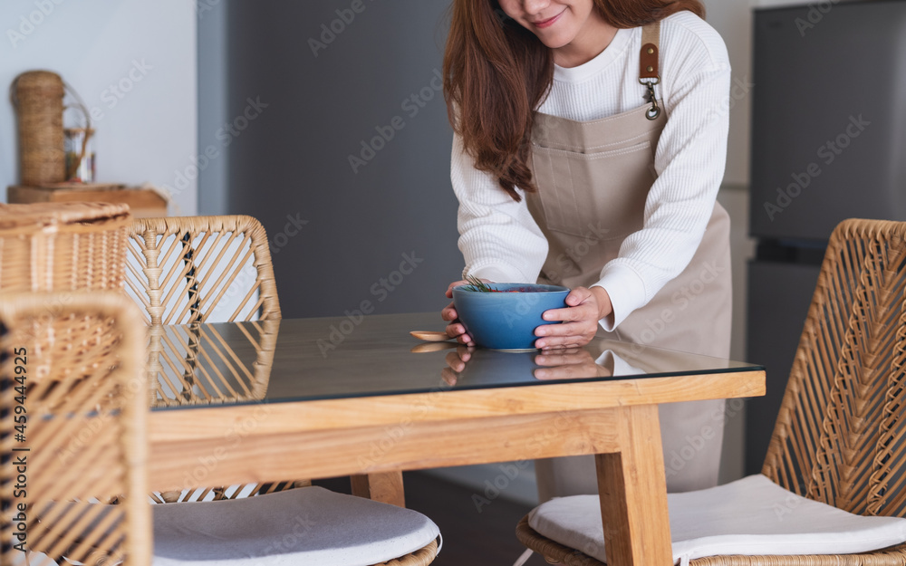 A woman  preparing and putting a bowl of food on dining table at home