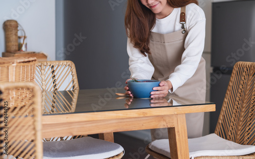 A woman preparing and putting a bowl of food on dining table at home