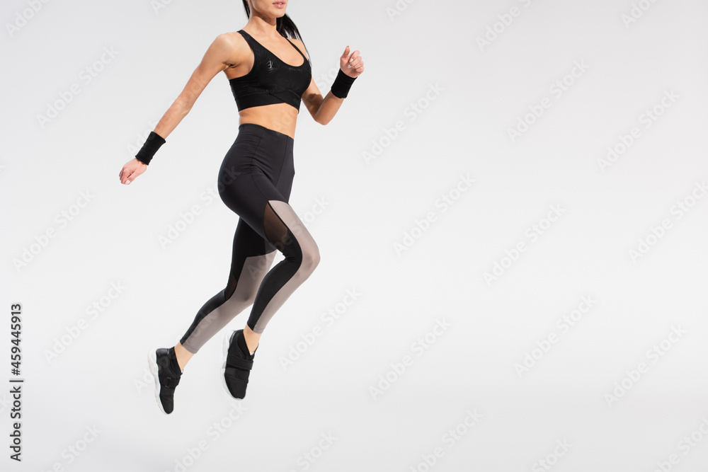 partial view of young woman in sportswear levitating on grey