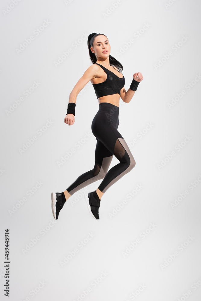 full length of young woman in sportswear levitating on grey