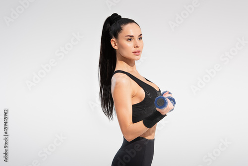 strong sportswoman in sportswear exercising with dumbbells isolated on grey © LIGHTFIELD STUDIOS