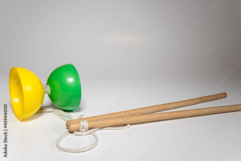 Diábolo de plástico amarillo y verde con dos palos de madera y una cuerda blanca listo para hacer malabares sobre un fondo blanco.
