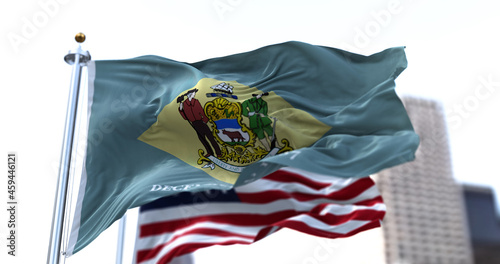 the flag of the US state of Delaware waving in the wind with the American stars and stripes flag blurred in the background